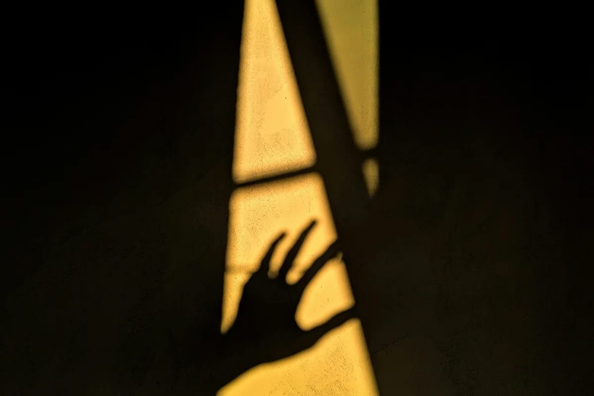 Hand silhouette caught in a shaft of warm light against a dark wall